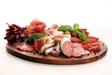 Food tray with delicious salami, pieces of sliced prosciutto crudo, sausage and basil. Meat platter with selection