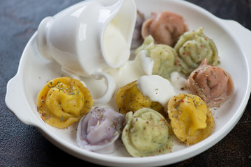 Closeup of boiled multicolored meat dumplings or pelmeni served with sour cream on a white plate