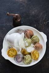 White plate with boiled colored dumplings pelmeni over dark brown stone background, vertical shot with copyspace