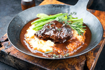Traditionelle deutsche geschmorte Kalbsbäckchen in brauner Rotwein Sauce mit Kartoffelpüree und Bohnen als closeup   in einer Eisenpfanne © HLPhoto