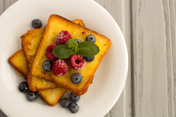 French toasts with berries and honey  in the white  plate on the grey wooden background.Top view.Copy space.
