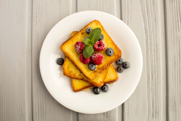 French toasts with berries and honey  in the white  plate on the grey wooden background.Top view.Copy space.