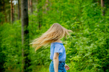 woman in blue blouse with long fluttering hair on nature background.Positive human emotions.long hair fluttering in motion.Young woman dancing in wild forest nature.girl flipping her hair from the