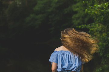 woman in blue blouse with long fluttering hair on nature background.Positive human emotions.long hair fluttering in motion.Young woman dancing in wild forest nature.girl flipping her hair from the