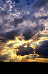 Wind generator turbines with dramatic sky. In the background you can see clouds and sunbeams. Renewable energy concept.