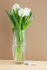 White tulips in a glass vase on a wooden table