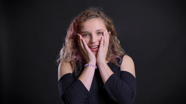 Portrait of young caucasian girl with pink hair watching into camera with amusement on black background.