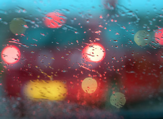 abstract pattern of colorful lights and rain drops during downpour on winshield of car