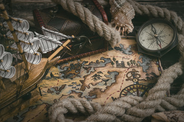 Pirate ship, treasure map, chest, compass and a mooring rope on a wooden table background.