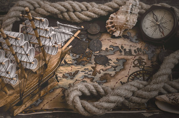 Pirate ship, treasure map, compass and a mooring rope on a wooden table background.