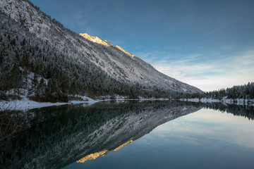 lake plansee at winter sunrise with mirroring alpine mountain in water