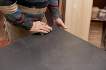 a man treats a black matte surface with a sponge with sandpaper.