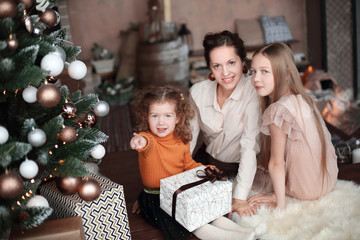 mother and her daughters opening a gift box near the Christmas tree