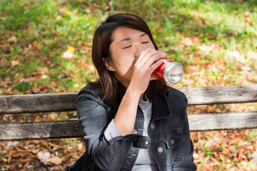 Chinese Girl Sitting on the Bench in a Park and Drinking Beer From the Can