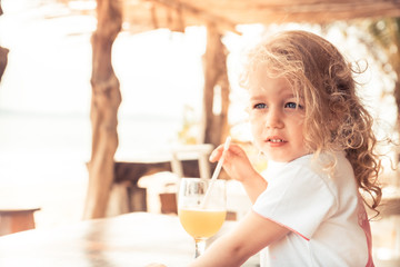 cute beautiful child girl enjoy drinking fresh juice in hot summer day looking into the distance during summer beach holidays with copy space