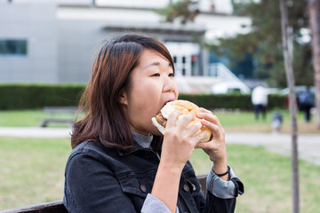 Chinese Girl Sitting on the Bench and Eating Hamburger