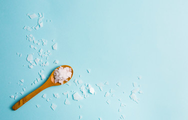 Magnesium Chloride Flakes scattered around brown wooden spoon on blue background. For making foot...