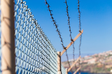 Mesh fence with barbed wire on a background of the blue sky