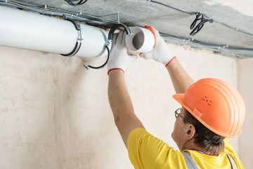 The worker is installing a ventilation system.