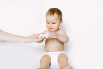 Hygiene - young momy wiping the baby skin with wet wipes. Little baby girl in diaper sitting and taking the wet wipe from mother hand. Cleaning wipe, pure, clean