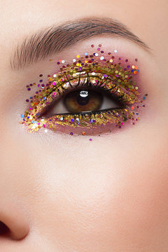 Beautiful macro shot of female eye with ceremonial makeup. Perfect shape of eyebrows, eyeliner and pretty gold gletter on eyelid. Cosmetics and make-up. Closeup macro shot of fashion sparcle visage