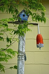 A birdhouse and buoy on a pole next to a house with yellow siding.