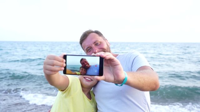 Closeup video portrait of happy family of two persons having fun at sea beach. Summer vacation in hotel resort. Father and son taking selfie using digital camera of modern smartphone. Focus at faces.