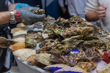 A man cleans oysters in shells with iron gloves.
