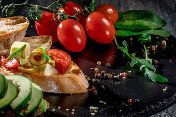 Fresh delicious bruschetti. Variety of small sandwiches with parmesan cheese, cherry tomato, egg, cucumber, avocado on rustic wooden board over dark background