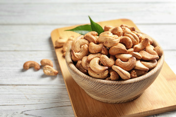 Bowl with cashew nuts on wooden table. Space for text
