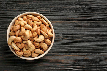 Bowl with cashew nuts on wooden table, top view. Space for text