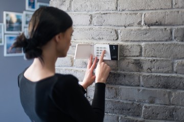 Young woman entering security pin on home alarm keypad.