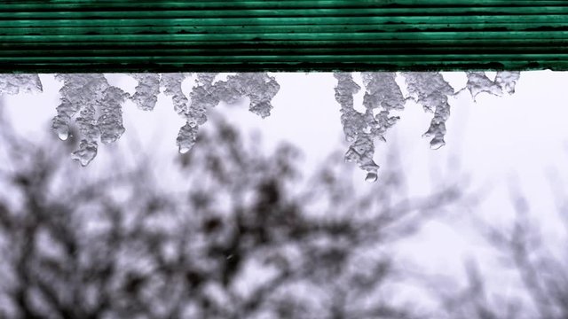 Spring Snow Melting on the Roof House. Close-up. Icicles hang from theshed, melt and drip. Warming.