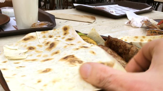 Hands of person who removes pita bread from dish in which vegetables and lula kebab from minced meat lie.