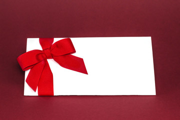 Gift isolated white card with red ribbon bow on deep red background.
