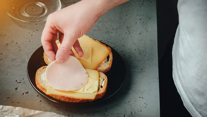 The man prepares sandwiches to eat. The concept of eating, preparing meals. The man puts the sausage on bread, on a stone dark background. Eating breakfast, dinner.