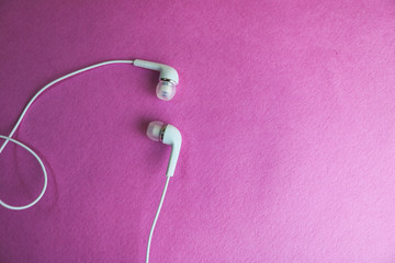 Beautiful modern digital plastic vacuum white headphones with wires for listening to music on a purple pink background. Copy space