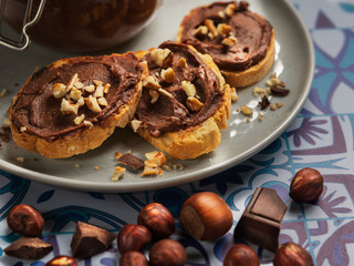 Homemade hazelnut cream in bowl with hazelnut nuts and slices of toast with chocolate cream on wooden background with copy space.