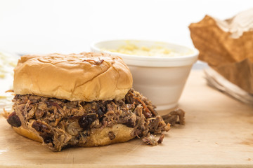 Meat spilling from BBQ Sandwich with takeout bag and Potato Salad in BG