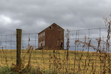 Obraz premium Sharp focus on wire fence with blurry abandoned farmhouse in distance