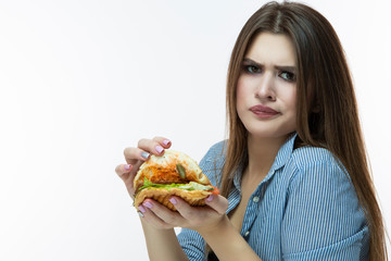 Fastfood Eating Concept. Young Caucasian Female Eating Burger With Displeasing facial Expression in Studio. Posing in Striped Shirt Indoors.