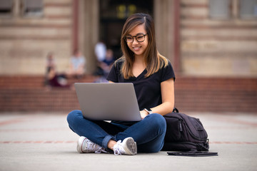 Cheerful young asian student working outdoors on laptop at university campus square © elnariz