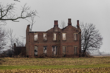 Old abandoned vintage mansion in middle of farm field with barren trees