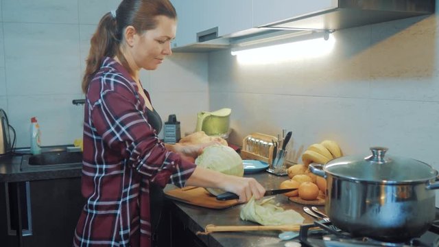 woman in the kitchen preparing a meal concept. girl in the kitchen cuts cabbage with a knife. cook vegetarian food healthy food. girl at home in the kitchen slow motion lifestyle video