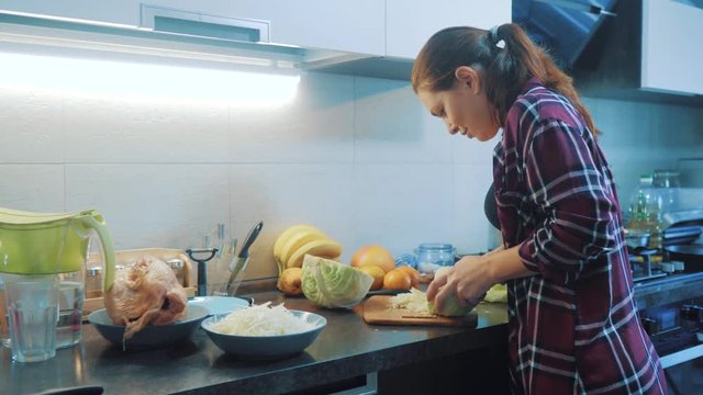 woman in the kitchen preparing a meal lifestyle concept. girl in the kitchen cuts cabbage with a knife. cook vegetarian food healthy food. girl at home in the kitchen slow motion video