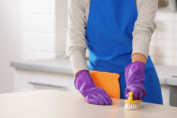 Woman cleaning table with brush in kitchen, closeup. Space for text