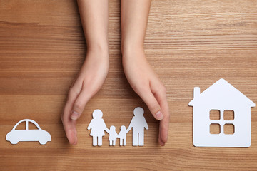 Woman holding hands over paper silhouette of family on wooden background, top view. Life insurance...