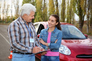 Naklejka premium Senior instructor with clipboard and woman outdoors. Get driving license
