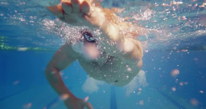 Professional swimmer with googles trains with effort and dedication to win the race by swimming in a freestyle pool. Shot with RED Camera in 8K. Concept of sport, swimming pool, competition, fitness.