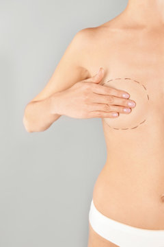 Young woman with marks on breast for cosmetic surgery operation against gray background, closeup